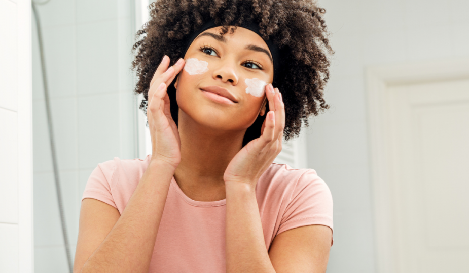 woman looking in mirror applying skincare products to cheeks